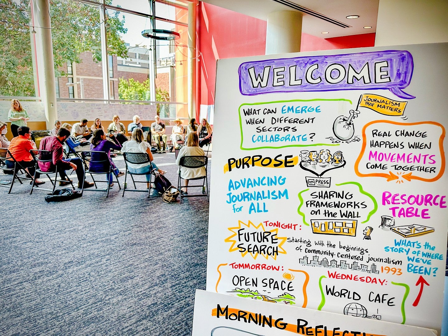 a colorful handwritten poster with notes about advancing journalism for all, with a group of people in the background