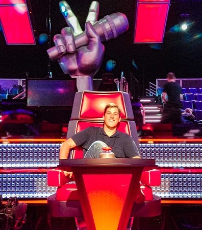 Alex Horwitch sits in a judge's chair from the Voice