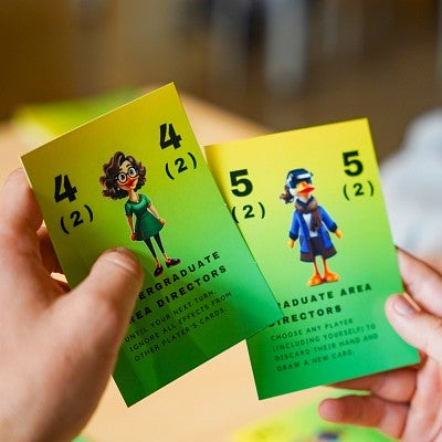 a person holds two cards from SOJC Letters, a game created in a media studies production class