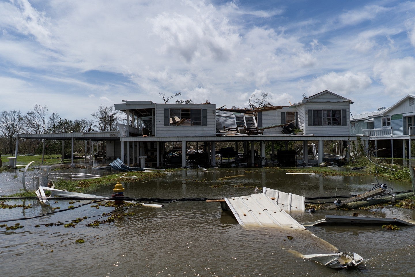 A road flooded with water and debris, and a damaged building in the background.