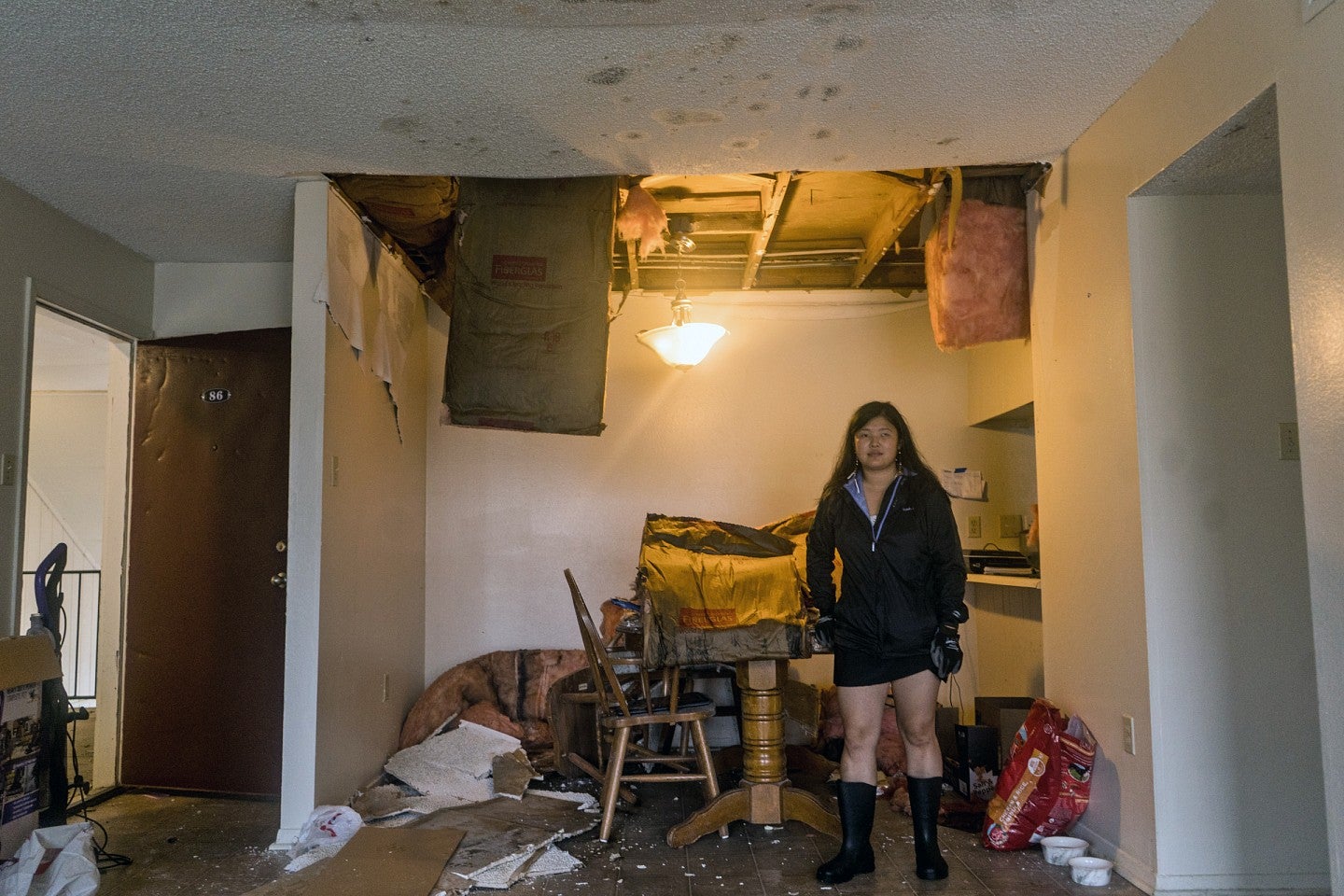 Kezia Setyawan stands in her ruined apartment building. The ceiling is damaged, with insulation falling onto the floor.