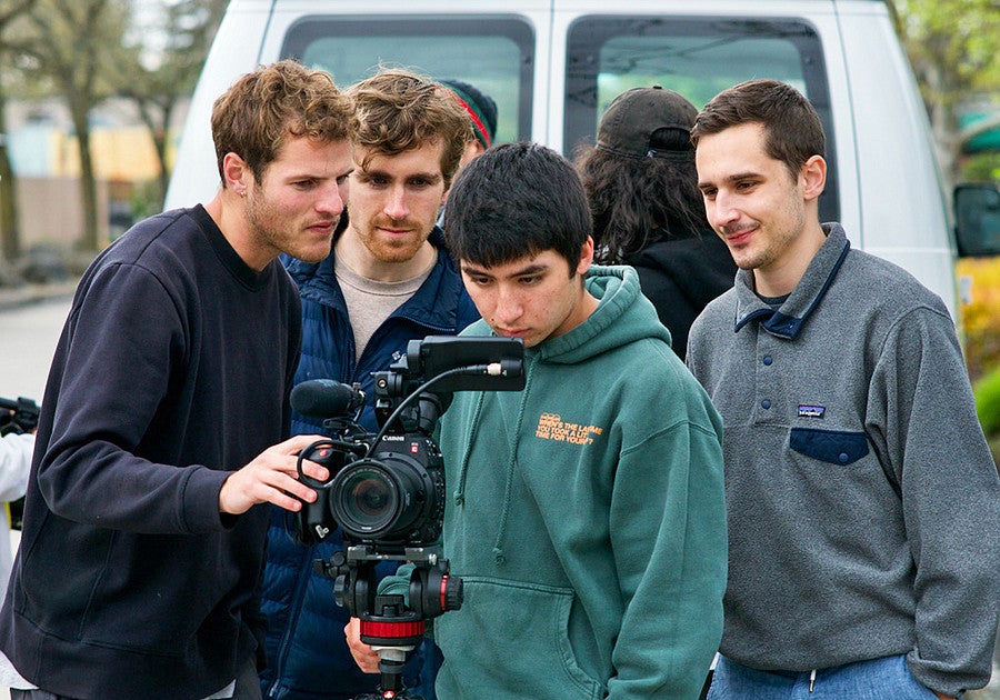 four people look into the viewfinder screen of a video camera