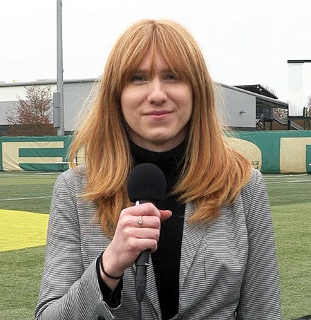 Cam Brown stands on a University of Oregon practice field holding a microphone