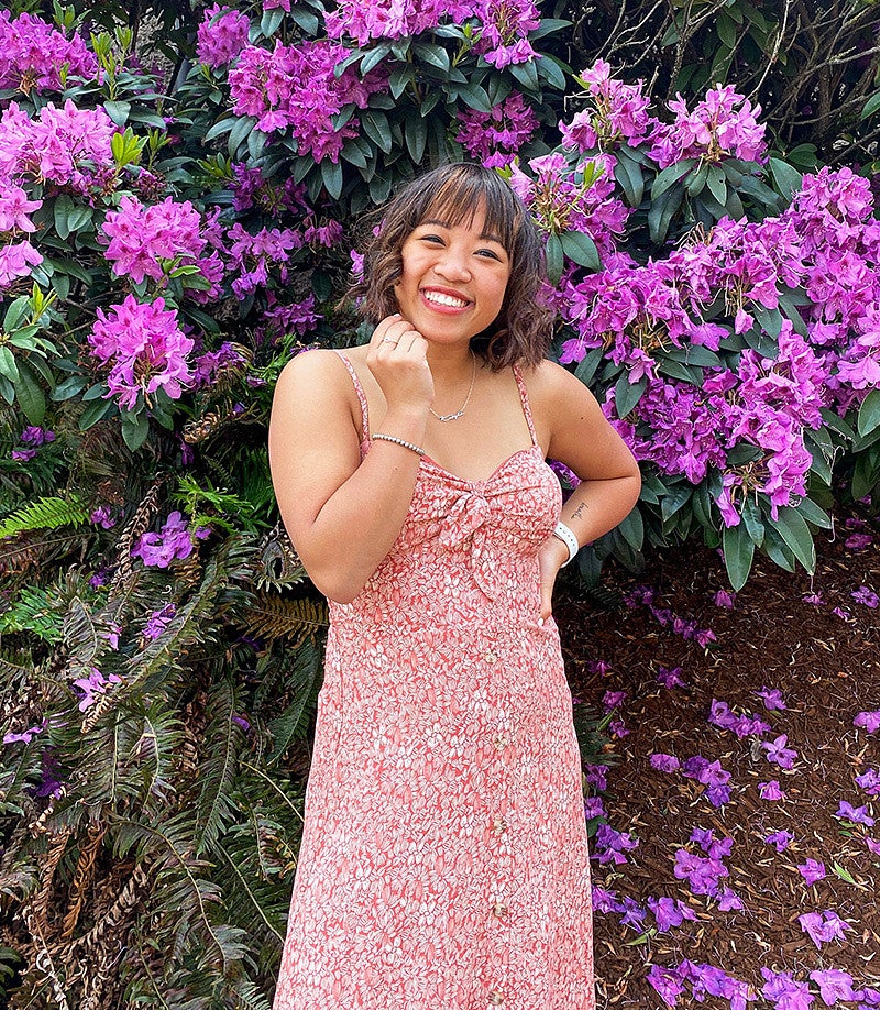 Kayla Nguyen stands in front of a flowering purple rhodedendron