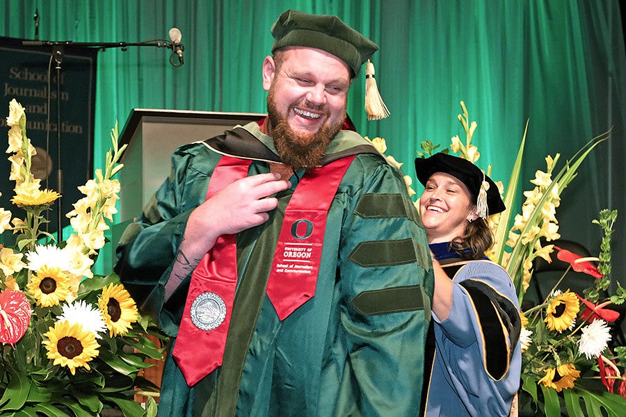 An SOJC student receiving a PhD is hooded by a professor at the 2022 commencement ceremony