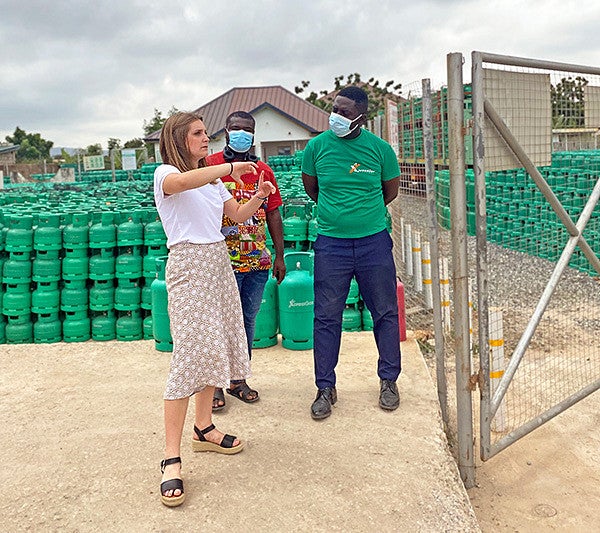 Liz Sgro gestures alongside two men wearing masks in front of hundreds of bright green gas canisters