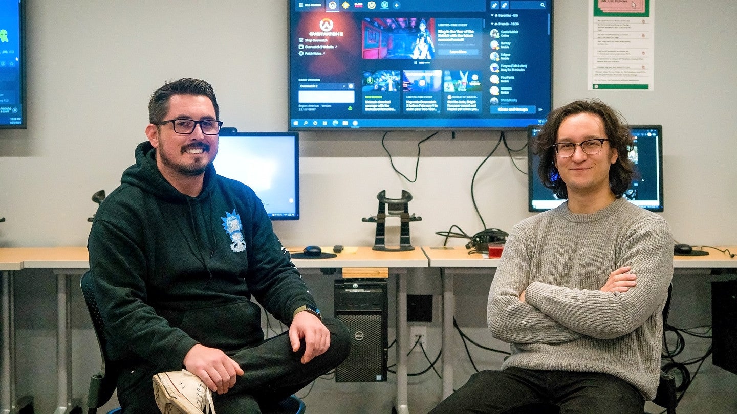 Two people sit in front of computer screens and monitors