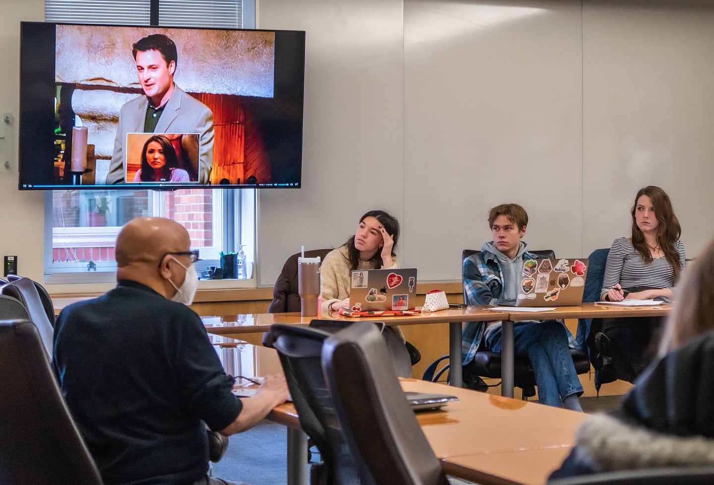 a professor and three students in class with a TV screen showing the Bachelor