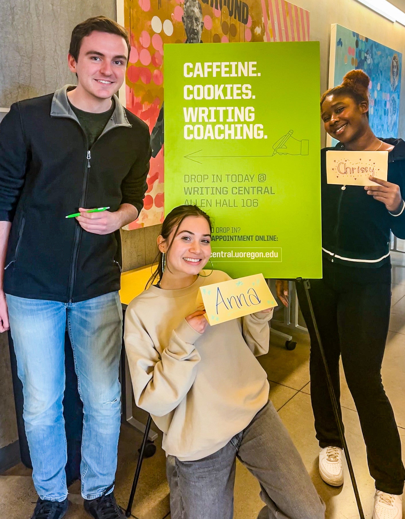 three students pose with a sign advertising Writing Central