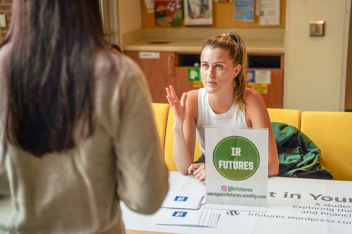 a student gestures while sitting behind a sign that says IR Futures