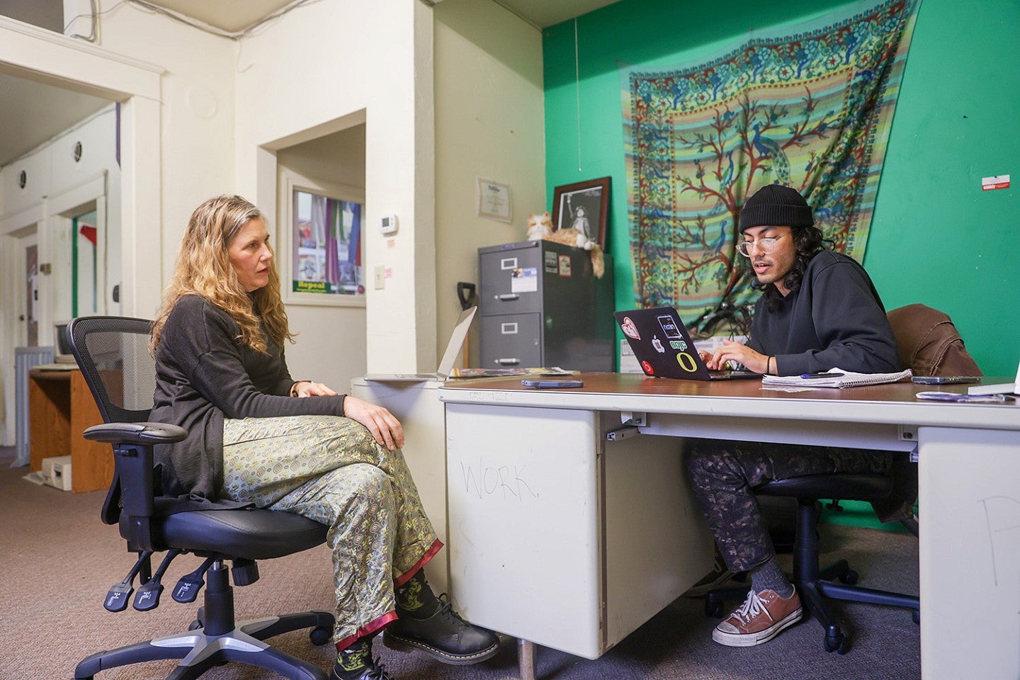 Camilla Mortensen and Faheem Kahn sit in office chairs and work on laptops across a desk from each other