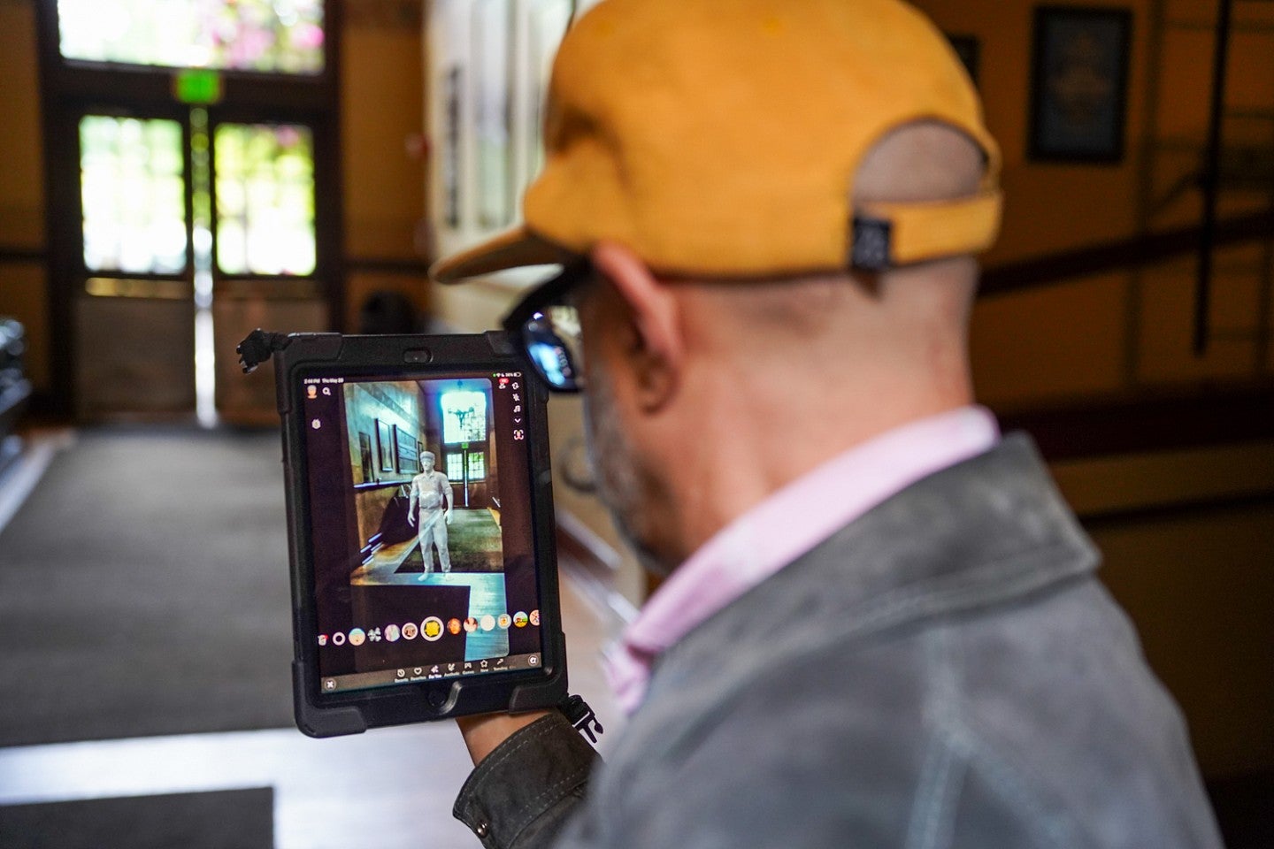 Jason de Parrie-Turner holds up a tablet showing an augmented reality project showing a digital ghost that appears to be standing in a hallway at McMenamin's Kennedy School in Portland.