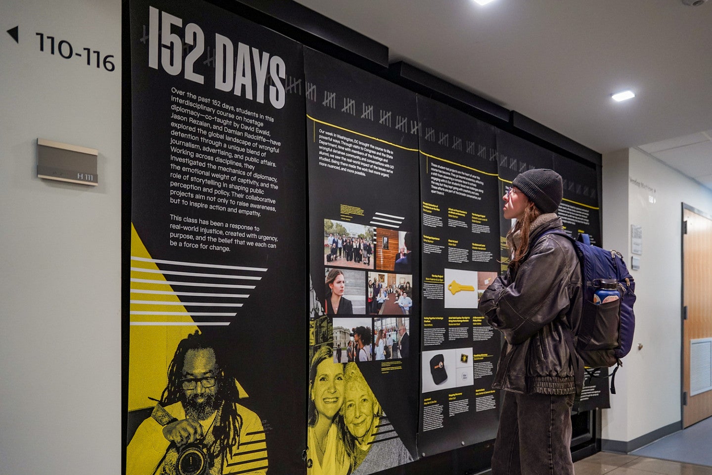 a student stands in front of a floor-to-ceiling wall display titled "152 Days" with text and photos on a black background