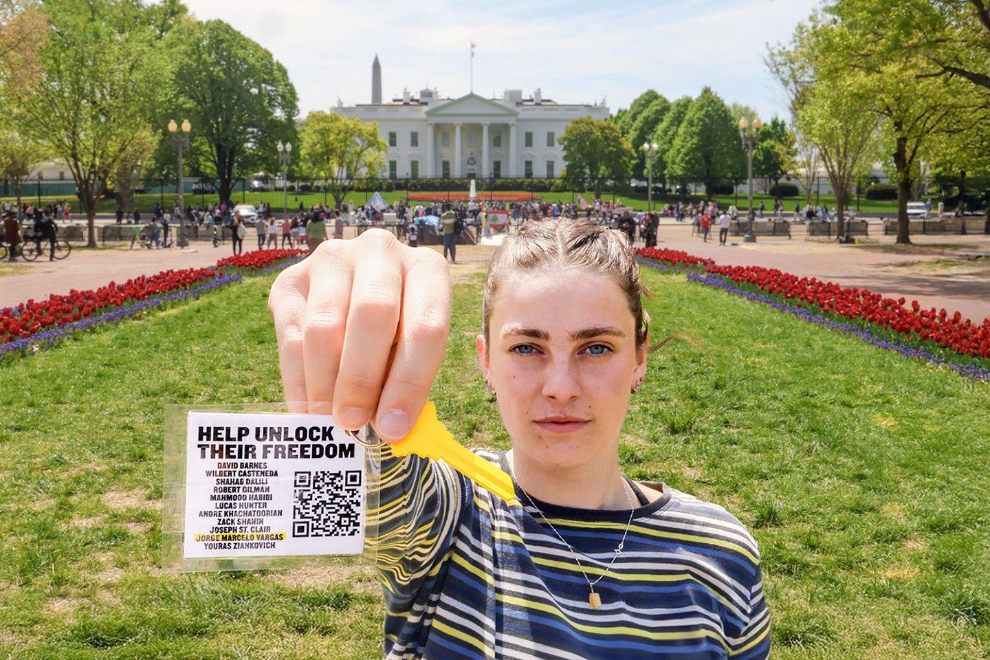 Maren Fullerton holds a white tag attached to a bright yellow key close to the camera; a green lawn and the White House are in the background