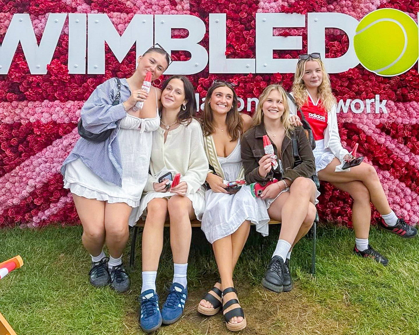 five students pose in front of a wall covered in pink flowers and a sign for Wimbledon