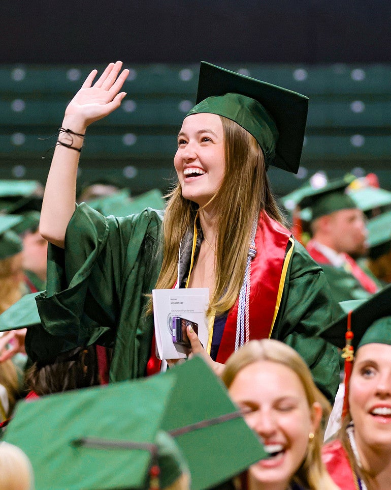 a university of oregon school of journalism and communication graduate waves during the commencement ceremony