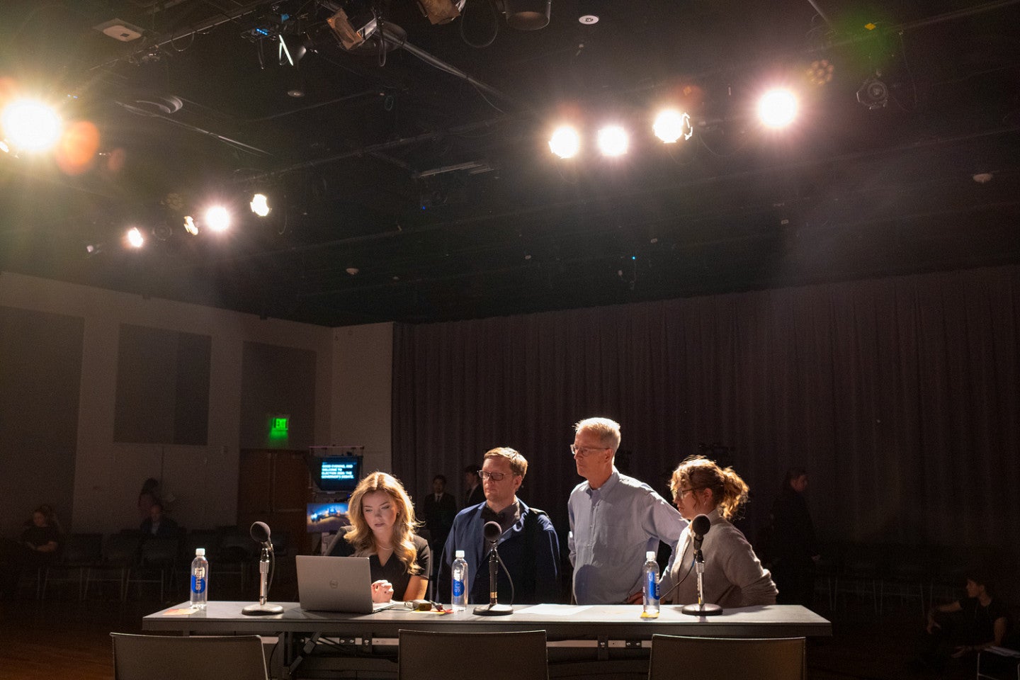 the moderator and panelists for an oregon gubernatorial debate prepare in a dark room lit with studio lights