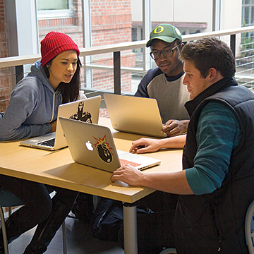 three students work at laptops around a table in Allen Hall
