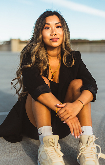 Nicole Lee sits on the ground wearing a black blazer, shorts, and white sneakers