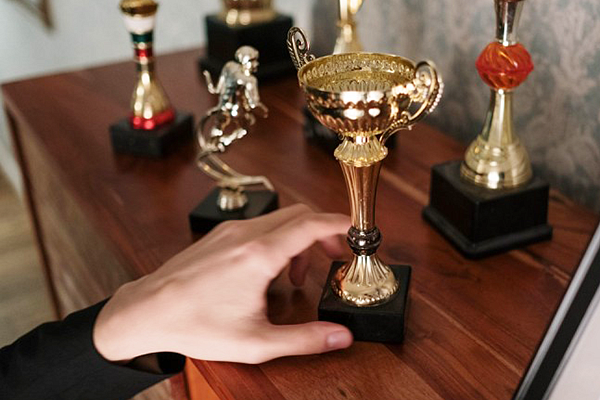 A hand reaching toward several trophies sitting on a dresser