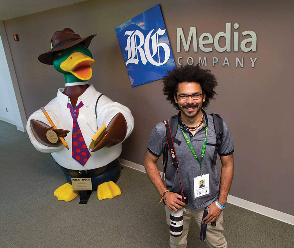 2021 Snowden intern Jeremy Williams poses with a large reporter duck sculpture and the RG media sign