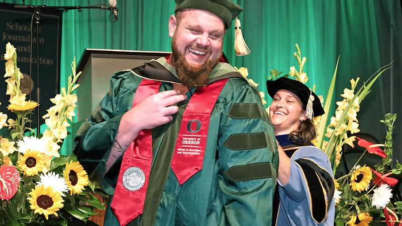 An SOJC student receiving a PhD is hooded by a professor at the 2022 commencement ceremony