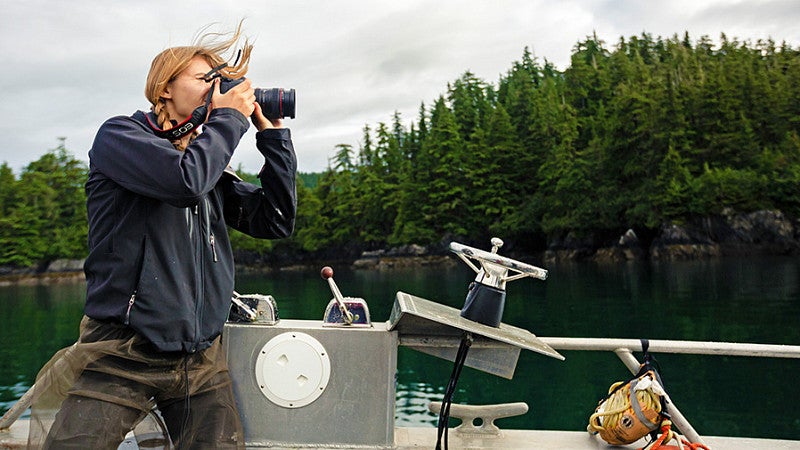 a person looks through the lens of a digital camera while standing in a boat on a lake