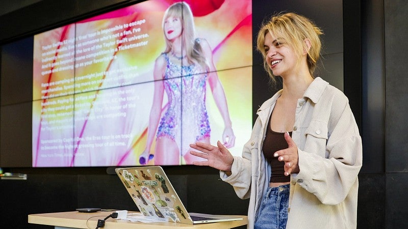a student presents research in front of a digital screen showing taylor swift