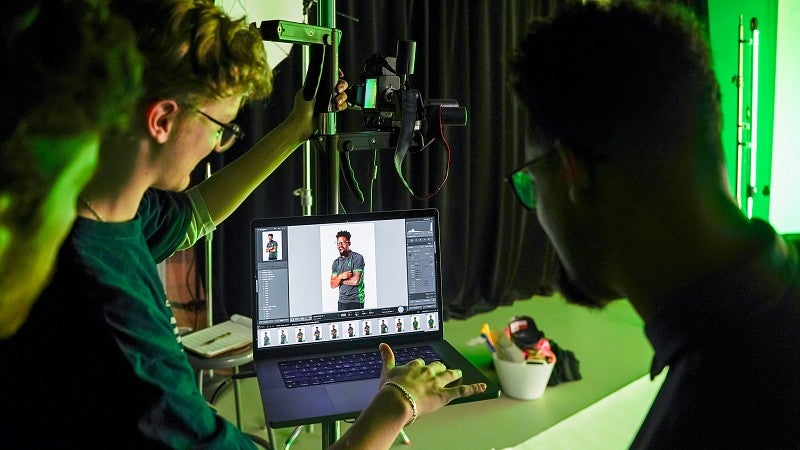 students look at a photoshoot on a laptop in a photo studio lit with green lights