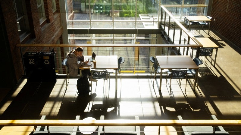 a student studies in the atrium of Allen Hall silhouetted by sunlight and long shadows