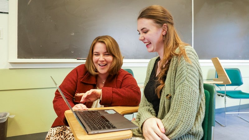 Megan Denneny kneels to look at the laptop of another seated graduate student