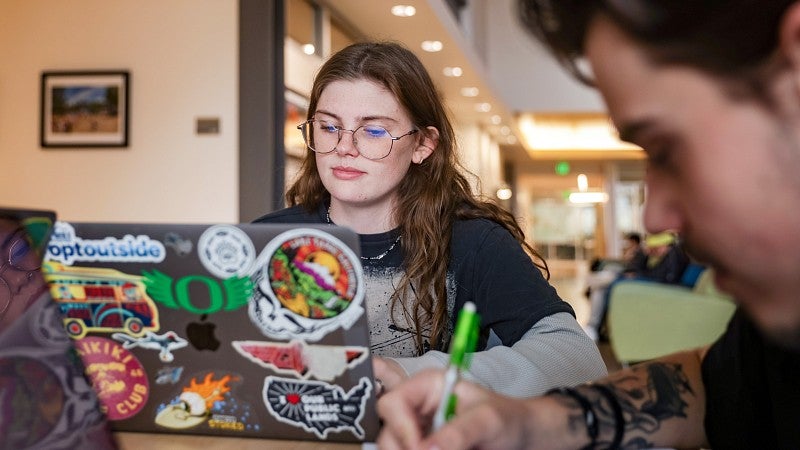 a student studies in Allen Hall with a laptop covered in colorful stickers