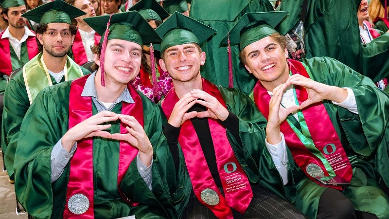 three students wearing green caps and gowns throw their Os