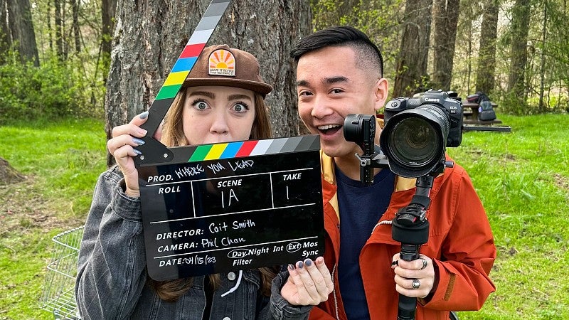 two SOJC students pose while holding a film clapper and a video camera