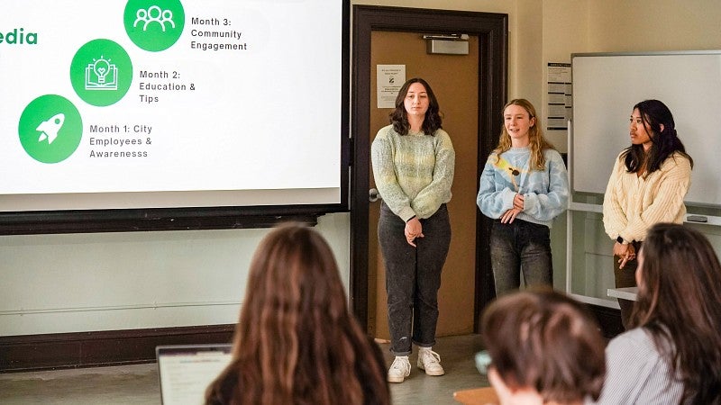 three PR students present a client proposal in front of a projector screen