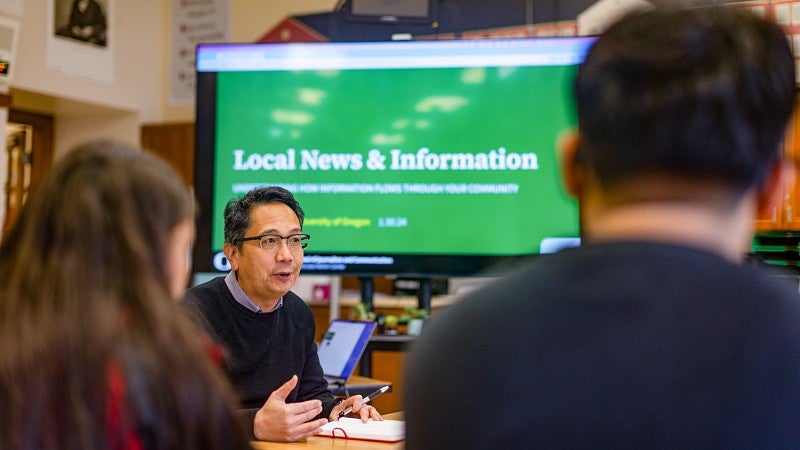 Andrew deVigal, director of the Agora Journalism Center, presents in front of a screen that says "Local News & Information" as he talks to students about community trust in media