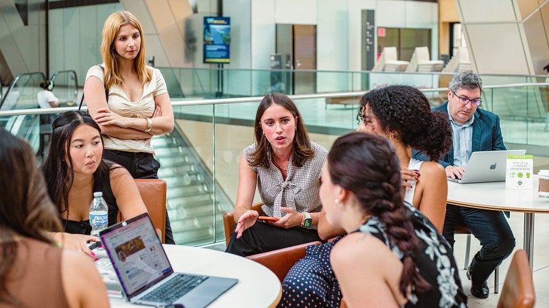 a group of students chat with a staff member in the atrium of the Hearst building in New York City