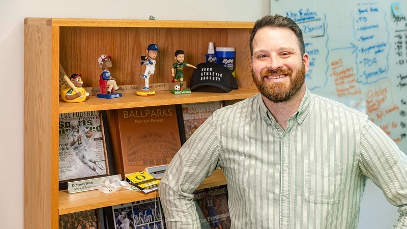 Sports PR expert Henry Wear poses in front of a bookcase full of baseball memorabilia