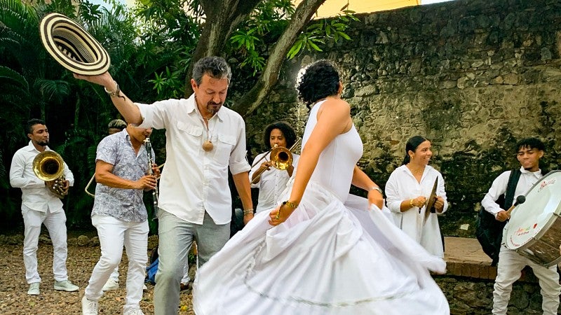 Juan-Carlos Molleda dances with someone wearing a swishy white skirt while people play instruments in the background