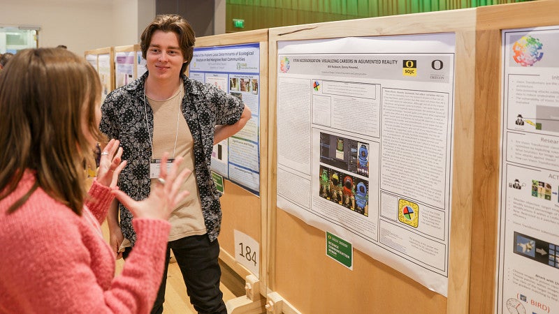 SOJC student Will Nussbaum presents his research poster to an audience member at the UO Undergraduate Research Forum