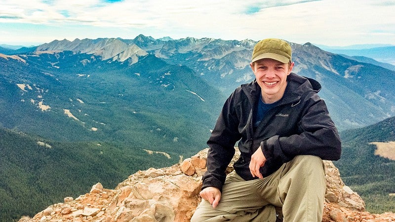 Travis Wilson poses on top of a mountain in Montana