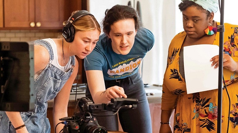 A group of three students work behind the scenes on a multimedia journalism video shoot