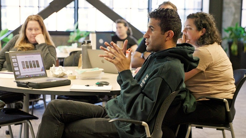 a strategic communication master's student gestures while sitting a table with other students during a class discussion