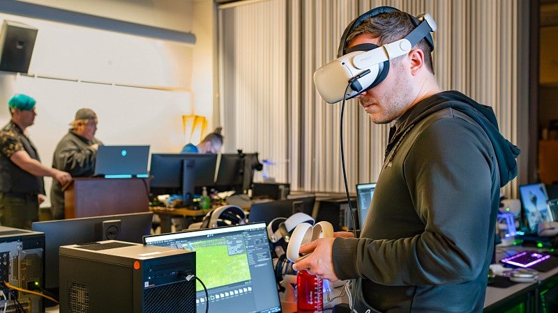 Luke Walker tests an immersive media project on his computer while wearing a VR headset