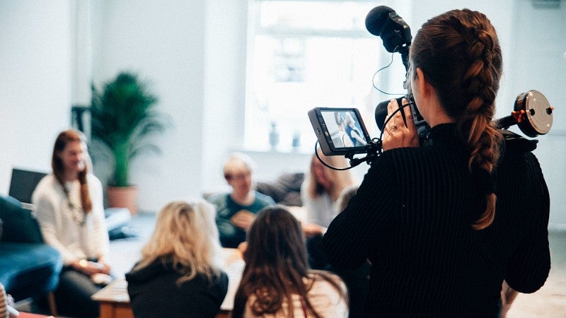 a person films a group of people having a discussion around a table