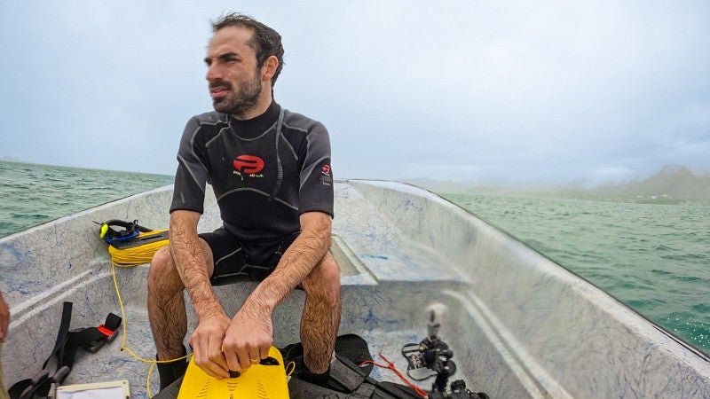 Sam Morrison sits in a small boat on the ocean while wearing a wetsuit