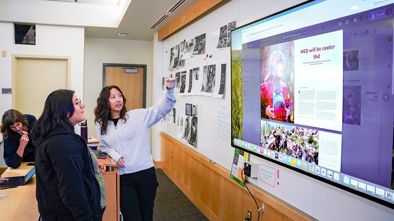 two students review an unfinished magazine spread displayed on a large digital screen