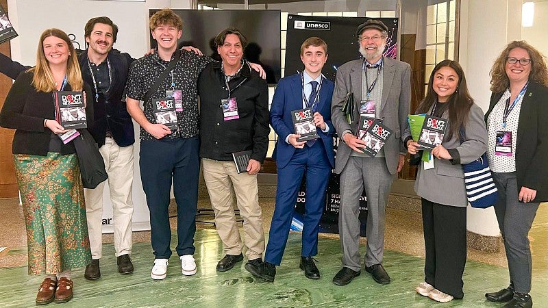 a group of University of Oregon students and professors pose while holding books