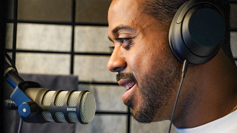 a close-up of Berto Jolliffe wearing headphones and speaking into a microphone in a recording studio