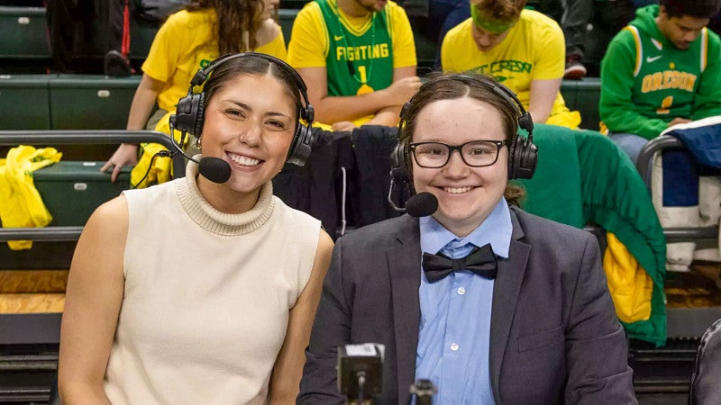 two female student broadcasters pose at an Oregon basketball game